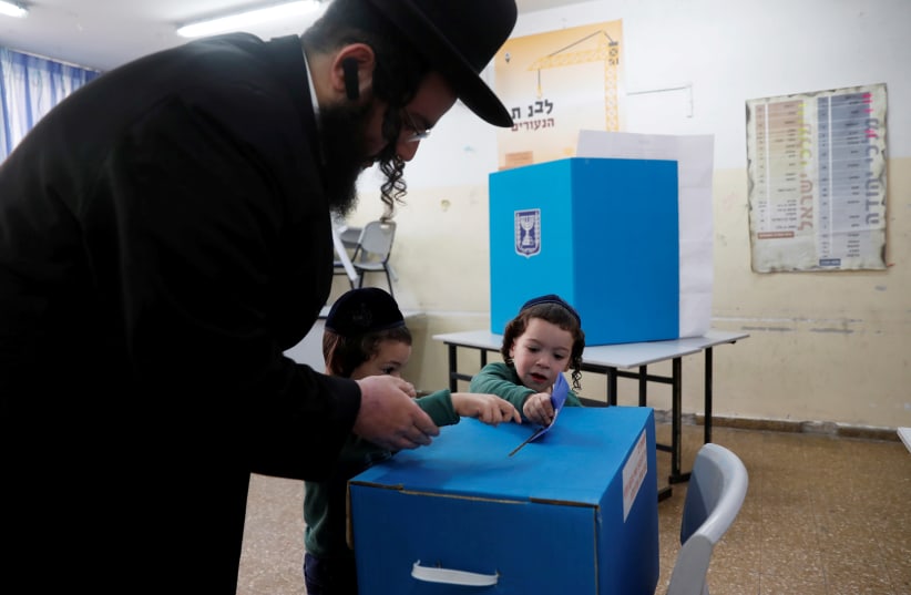 An ultra-Orthodox Jewish man helps kids cast his ballot at a polling station as Israelis vote in a parliamentary election, in Jerusalem April 9, 2019 (photo credit: RONEN ZVULUN/REUTERS)