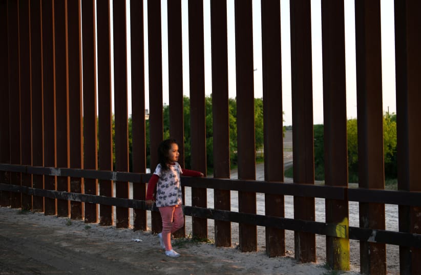 Young Central American migrant girl seeking asylum walks along border fence (photo credit: LOREN ELLIOTT/REUTERS)