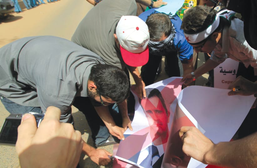 People burn a picture of Syrian President Bashar Assad during a protest outside the Syrian embassy in Khartoum, Sudan in 2012 (photo credit: REUTERS)