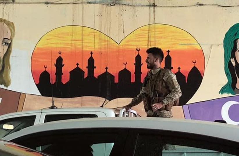 An Iraqi Popular Mobilisation Forces (PMU) member rides on the back of a pickup truck past a Shi’ite mural in Baghdad, Iraq (photo credit: REUTERS/MARIUS BOSCH)