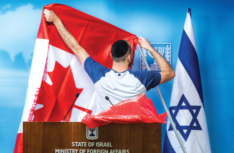 A MAN adjusts a Canadian flag next to an Israeli flag before a diplomatic meeting.  (photo credit: REUTERS)