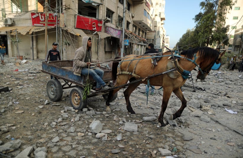 A Palestinian rides a horse-drawn cart through a debris-strewn street near a building destroyed by Israeli air strikes, in Gaza City May 5, 2019 (photo credit: SUHAIB SALEM / REUTERS)