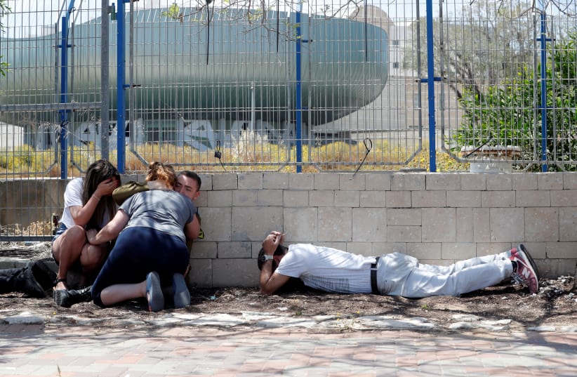 sraelis take cover as they hear sirens warning of incoming rockets from Gaza, during cross-border hostilities, in the southern Israeli city of Ashkelon (photo credit: RONEN ZVULUN/REUTERS)
