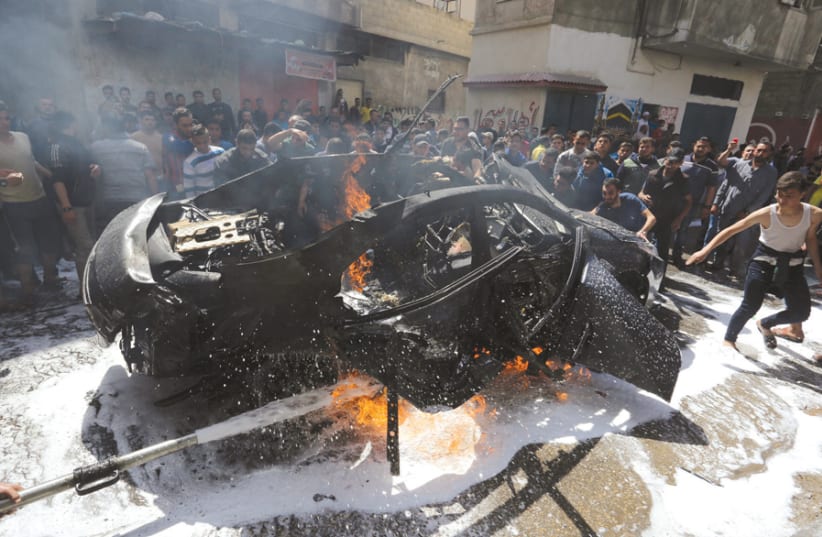 Palestinians try to extinguish a fire in the car of a Hamas commander who was killed in an Israeli air strike on Gaza City, on May 5 (photo credit: ASHRAF ABU AMRAH / REUTERS)
