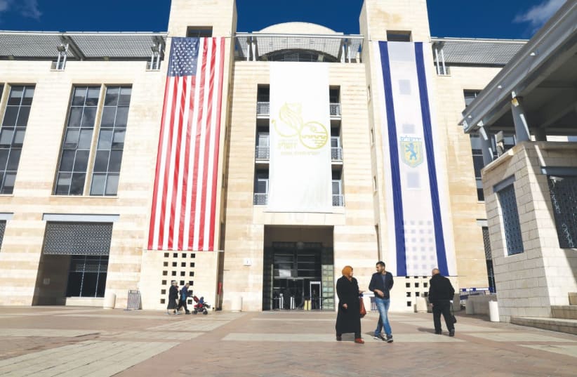 PEOPLE WALK at Jerusalem’s City Hall as the American and Jerusalem flags hang on the municipality building in 2017. (photo credit: AMMAR AWAD / REUTERS)