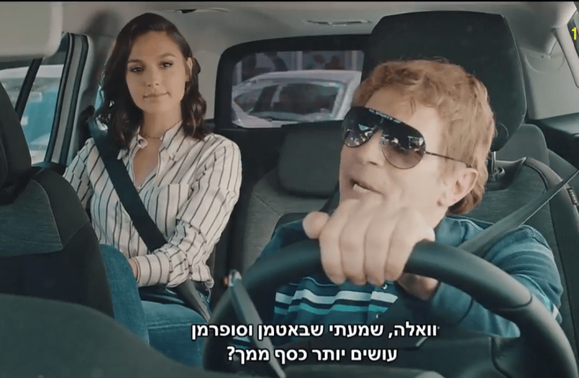 Gal Gadot sits in the back of a cab with driver Yuval Semo in her Eurovision video appearance (photo credit: SCREENSHOT/KAN)