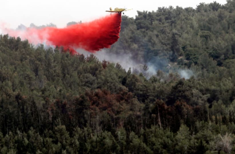 A firefighting aircraft flies over a forest near kibbutz Harel which was damaged by wildfires during a record heatwave, in Israel May 24, 2019. (photo credit: RONEN ZVULUN / REUTERS)