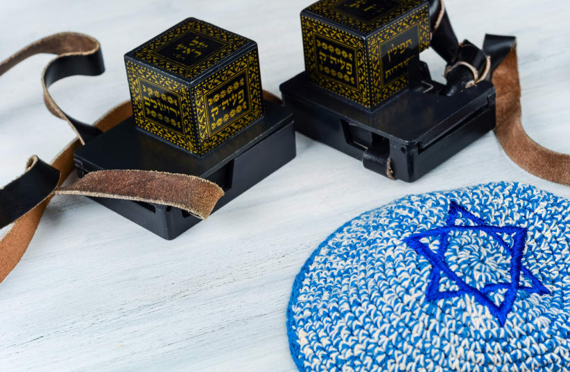 Pair of tefilin with black straps with blue kippah on white wooden background. (illustrative) (photo credit: INGIMAGE)