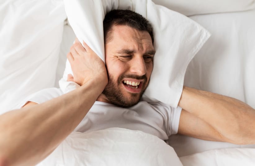 Man lying in bed with pillow suffering from noise  (photo credit: INGIMAGE)