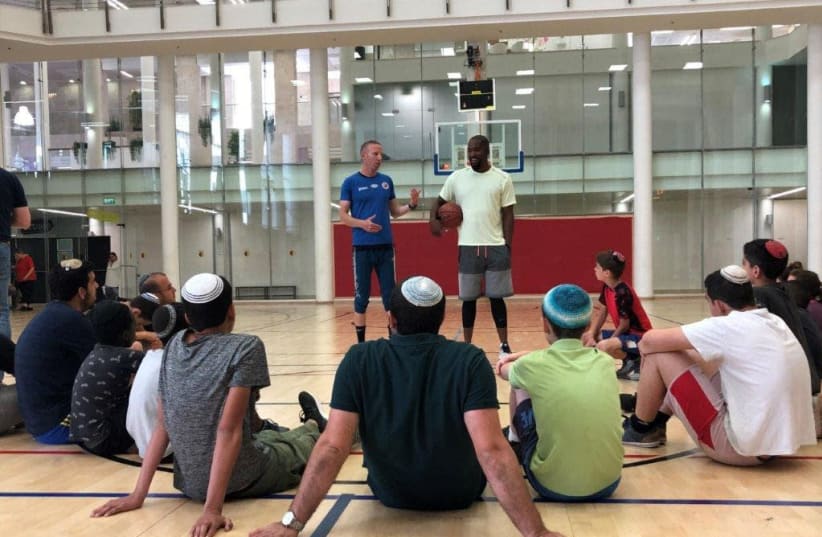 Basketball greats Tamir Goodman, left, and Michael Redd (right) conducting a basketball clinic for residents of World Emunah’s Neve Landy Children’s Village at the Jerusalem YMCA, May 2019 (photo credit: YAEL COHENCA)