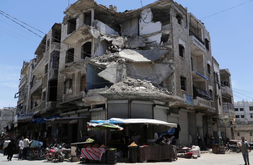 People walk past a damaged building in the city of Idlib on May 31, 2019. (photo credit: KHALIL ASHAWI / REUTERS)