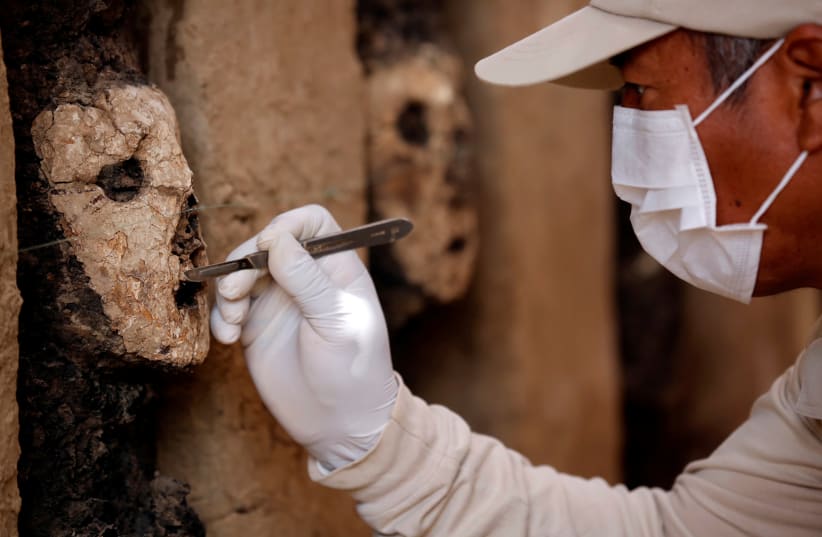 An archaeologist cleans a wooden mask of the Mochica culture at Chan Chan archeological complex in Trujillo, Peru October 22, 2018. (photo credit: DOUGLAS JUAREZ / REUTERS)