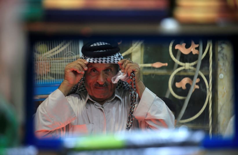 A man is seen reflected in a mirror as he buys a keffiyeh, a traditional Arabic headdress, at a store in a market in Najaf (photo credit: ALAA AL-MARJANI/REUTERS)