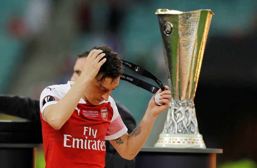 Arsenal's Mesut Ozil looks dejected as he walks past the Europa League trophy (photo credit: REUTERS)