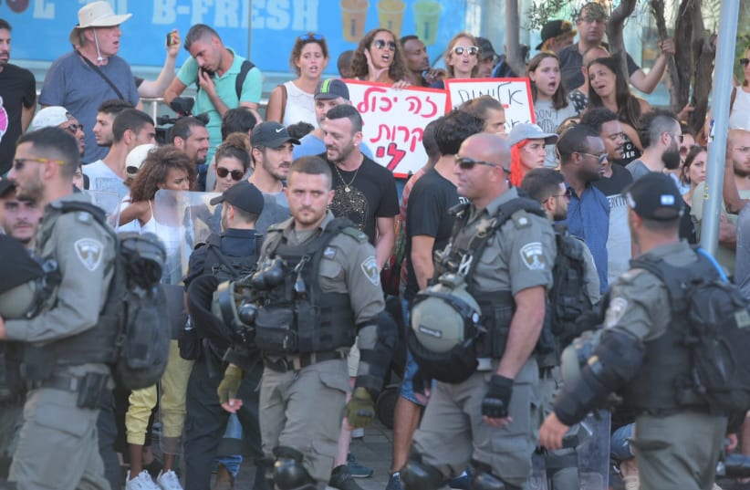 A protester holding a sign saying 'It could happen to me' as police officers walk by  (photo credit: AVSHALOM SASSONI)
