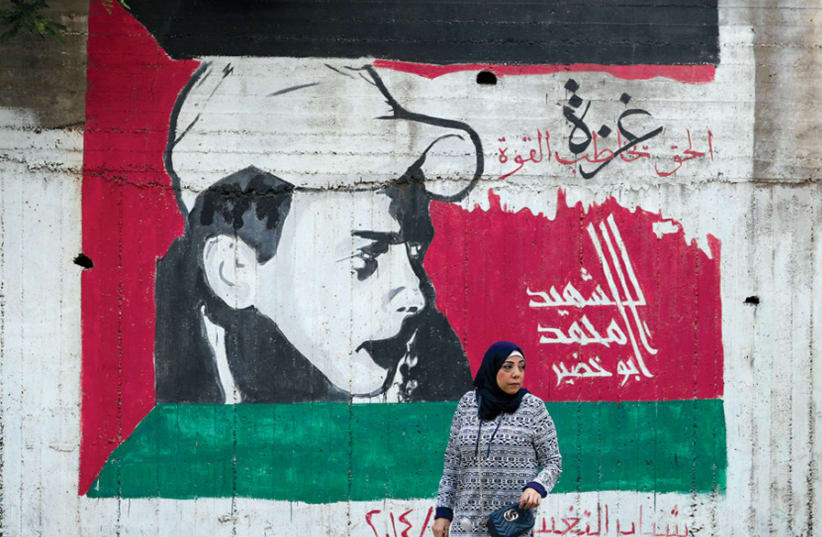 A WOMAN walks past a mural painted in the colors of the Palestinian flag, in Nazareth on May 9. (photo credit: AMMAR AWAD / REUTERS)