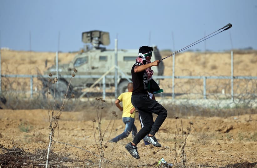 A Palestinian demonstrator uses a sling to hurl stones at Israeli forces during a protest at the Israel-Gaza border fence, in the southern Gaza Strip June 21, 2019 (photo credit: IBRAHEEM ABU MUSTAFA / REUTERS)