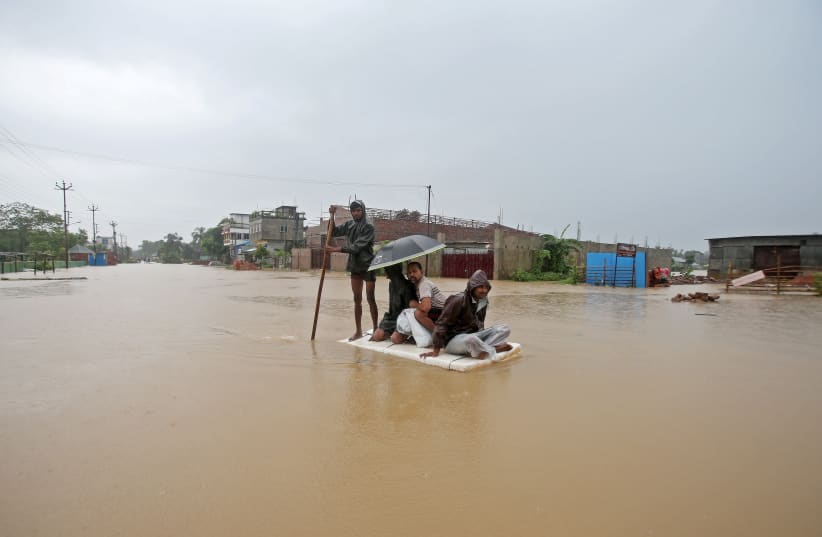 Villagers use a makeshift raft to cross a flooded area on the outskirts of Agartala, India July 15, 2019 (photo credit: REUTERS/JAYANTA DEY)