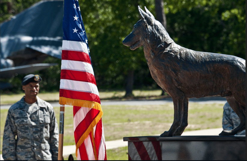 A security forces Airman stands with his military working dog behind the MWD memorial monument during a ceremony May 17 at the Air Armament Museum at Eglin Air Force Base, Fla.  (photo credit: US AIR FORCE)