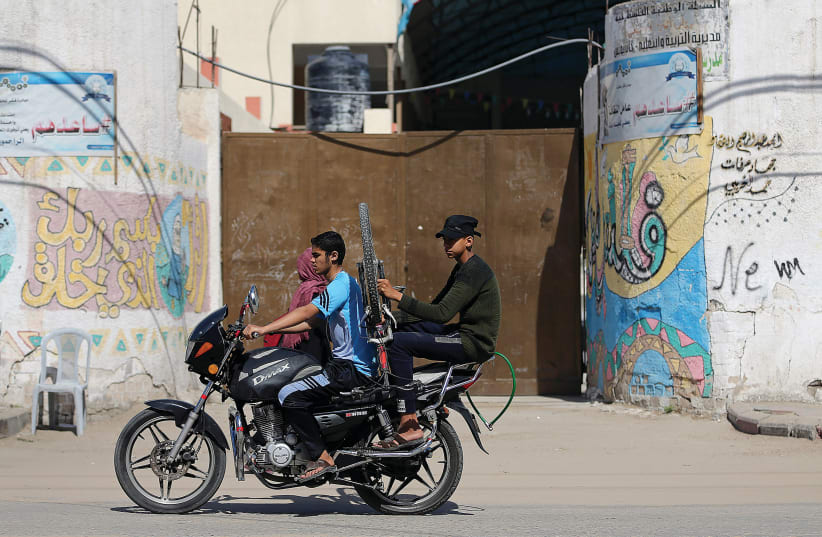 Youths ride a motorcycle past a closed school in the southern Gaza Strip in May.  (photo credit: IBRAHEEM ABU MUSTAFA / REUTERS)