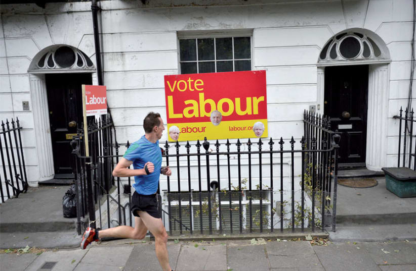 A man runs past a Labour Party sign with pictures of both Jeremy Corbyn and Britain’s new prime minister, Boris Johnson, in north London (photo credit: HANNAH MCKAY/ REUTERS)