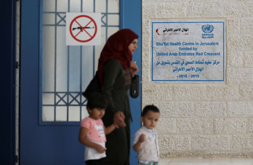A Palestinian woman walks with her children near an entrance of the UNRWA (United Nations Relief and Works Agency) health center in the Shuafat refugee camp in east Jerusalem October 10, 2018 (photo credit: AMMAR AWAD / REUTERS)