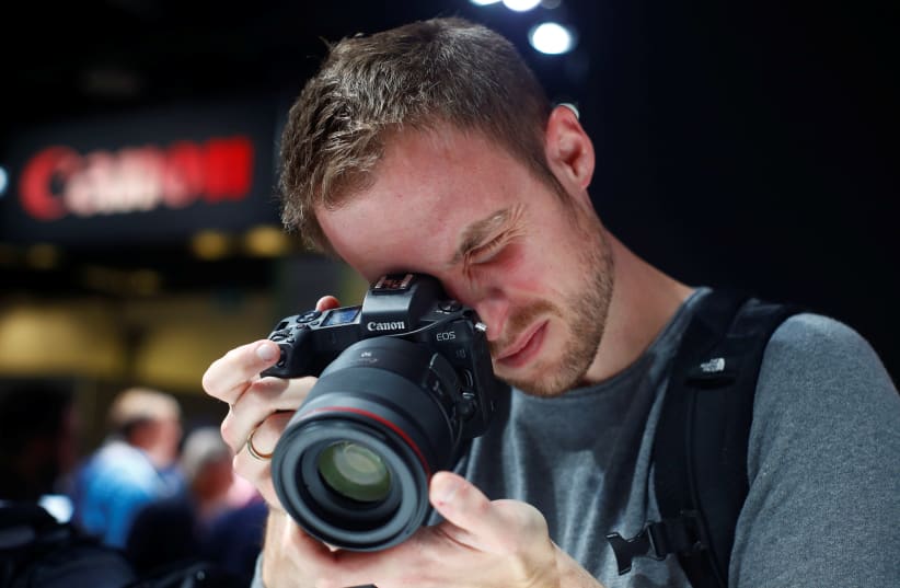 A visitor looks through Canon's first full-frame mirrorless digital camera, Eos R, during the first day of Photokina trade fair in Cologne, Germany September 26, 2018 (photo credit: REUTERS/WOLFGANG RATTAY)