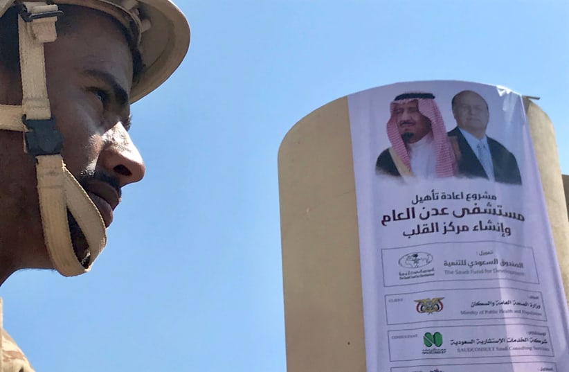 Yemeni soldier near a poster portraying Saudi Arabia's King Salman bin Abdulaziz Al Saud and Yemen's President Abdrabbuh Mansur Hadi outside a hospital renovated by Saudi Arabia in Aden (photo credit: NAEL SHYOUKHI/REUTERS)