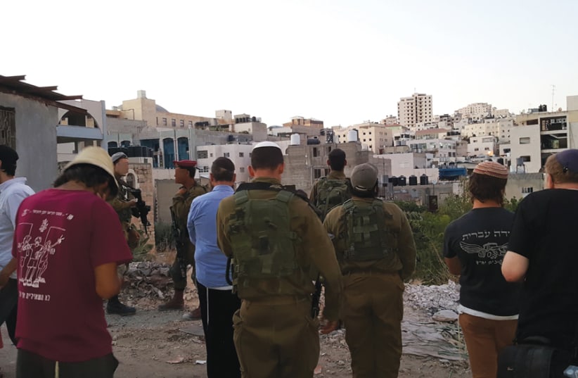 IDF SOLDIERS and visitors pray with Hebron’s shopping malls in the distance. (photo credit: BEN BRESKY)