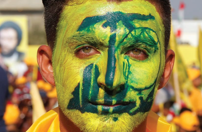A SUPPORTER with the Hezbollah logo painted on his face poses for a picture during a rally marking the 10th anniversary of the end of the 2006 war, in Bint Jbeil, southern Lebanon, on August 13, 2016. (photo credit: AZIZ TAHER/REUTERS)