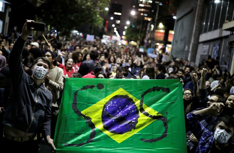Protesters hold a Brazilian flag with the letters SOS written on it during a demonstration to demand for more protection for the Amazon rainforest, in Sao Paulo, Brazil, August 23, 2019 (photo credit: NACHOS DOCE / REUTERS)
