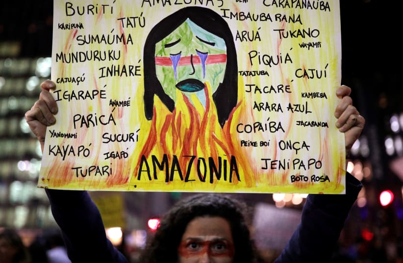 A protester holds a sign with the names of various indigenous tribes during a demonstration to demand for more protection for the Amazon rainforest, in Sao Paulo, Brazil, August 23, 2019 (photo credit: NACHOS DOCE / REUTERS)