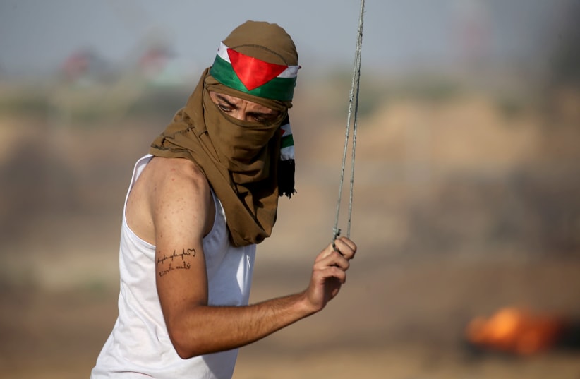 A Palestinian demonstrator uses a sling to hurl stones at Israeli forces during an-anti Israel protest at the Israel-Gaza border fence in the southern Gaza Strip August 23, 2019 (photo credit: IBRAHEEM ABU MUSTAFA / REUTERS)