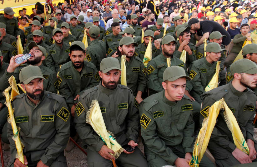 Lebanon's Hezbollah members hold party flags as they listen to their leader Sayyed Hassan Nasrallah addressing his supporters via a screen during a rally marking the anniversary of the defeat of militants near the Lebanese-Syrian border, in al-Ain village, Lebanon August 25, 2019.  (photo credit: REUTERS)