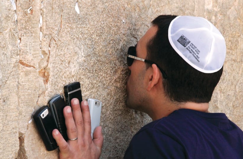 A visitor prays at the Western Wall, holding four cellphones (photo credit: MARC ISRAEL SELLEM)