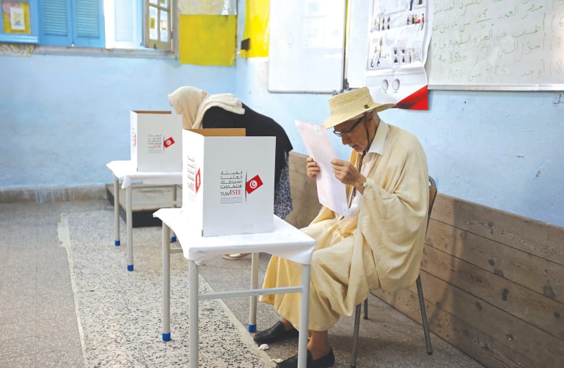 A MAN READS his ballot paper at a polling station during the presidential election in Tunis yesterday.  (photo credit: MUHAMMAD HAMED / REUTERS)