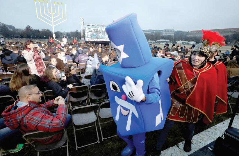 PITCHES TO Jews in America about their practice are diverse – Dreidel Man is escorted by Maccabee-costumed men before the National Menorah ceremony to mark Hanukkah near the White House, December 2018. (photo credit: YURI GRIPAS / REUTERS)