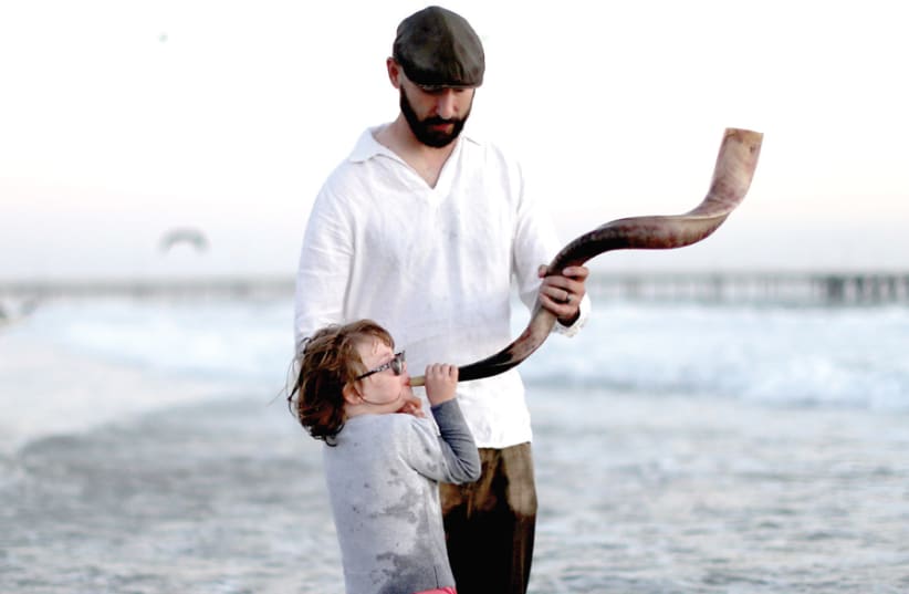 THE SHOFAR and prayers are supposed to help us with introspection but that is not always easy. A father holds a shofar for his daughter to blow. (photo credit: LUCY NICHOLSON / REUTERS)
