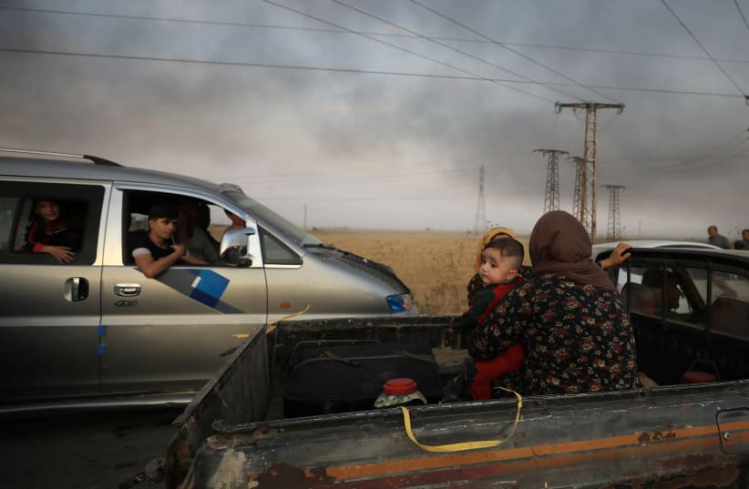 A woman with a baby sits at a back of a truck as they flee Ras al Ain town (photo credit: REUTERS/RODI SAID)