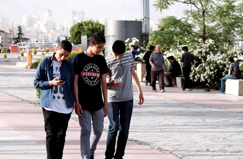Iranian youth use their mobile phones as they walk at a park in Tehran (photo credit: REUTERS)