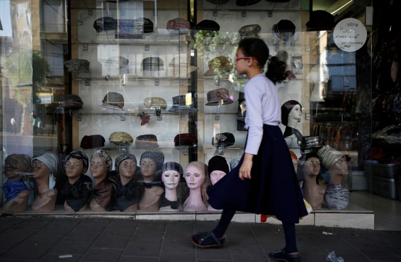 An ultra-Orthodox Jewish girl walks past a shop window displaying women's head coverings in Bnei Brak, Israel July 18, 2017. Picture taken July 18, 2017 (photo credit: REUTERS/AMIR COHEN)