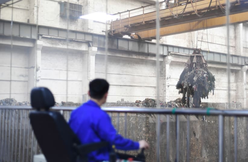 A worker operates a crane lifting garbage for incineration at a waste-to-energy plant in Kaili, Qiandongnan Miao and Dong Autonomous Prefecture, Guizhou province, China June 2, 2019. Picture taken June 2, 2019 through a glass window (photo credit: REUTERS/STRINGER)