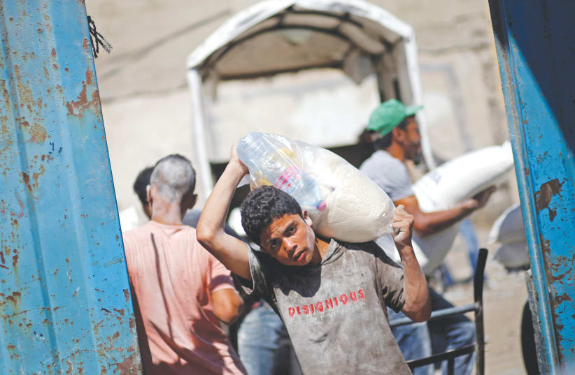 A PALESTINIAN carries food supplies at a Gaza aid distribution center run by the United Nations Relief and Works Agency (UNRWA), in the Al-Shati refugee camp (photo credit: MOHAMMED SALEM/REUTERS)