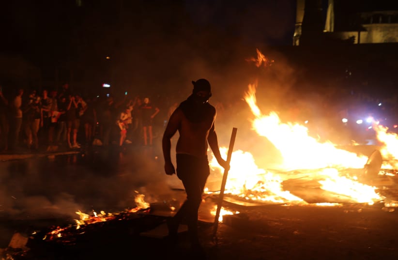 A demonstrator walks near a fire blocking a road during a protest targeting the government over an economic crisis, in downtown Beirut, Lebanon October 18, 2019.  (photo credit: HASAN SHAABAN/ REUTERS)
