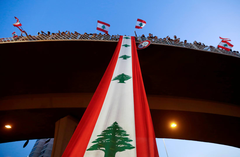 Demonstrators stand on a bridge decorated with a national flag during an anti-government protest along a highway in Jal el-Dib, Lebanon, October 21, 2019 (photo credit: MOHAMED AZAKIR / REUTERS)