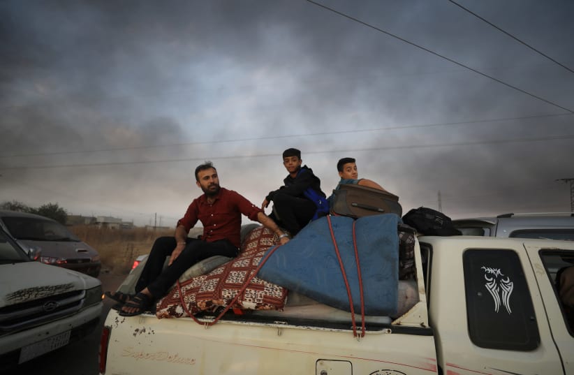 People sit on belongings at a back of a truck as they flee Ras al Ain in Syria. (photo credit: REUTERS)