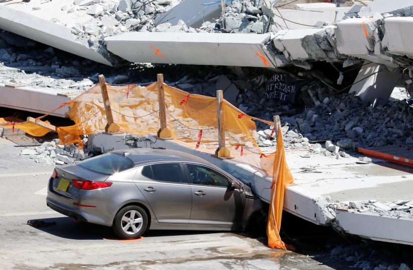 A damaged car is seen partially trapped as workers remove debris from a collapsed pedestrian bridge at Florida International University in Miami, Florida, U.S., March 16, 2018. (photo credit: REUTERS/JOE SKIPPER)