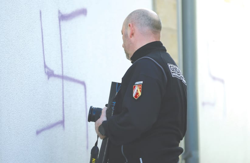 A FRENCH gendarme inspects swastikas painted on a wall of a former synagogue turned into a cultural center in Mommenheim near Strasbourg. (photo credit: REUTERS)