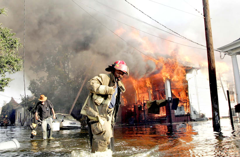 A FIREMAN helps a man as a home burns in New Orleans during the aftermath of Hurricane Katrina in 2005. The book follows family members of a dead villain, including their experiences related to the hurricane. (photo credit: REUTERS)