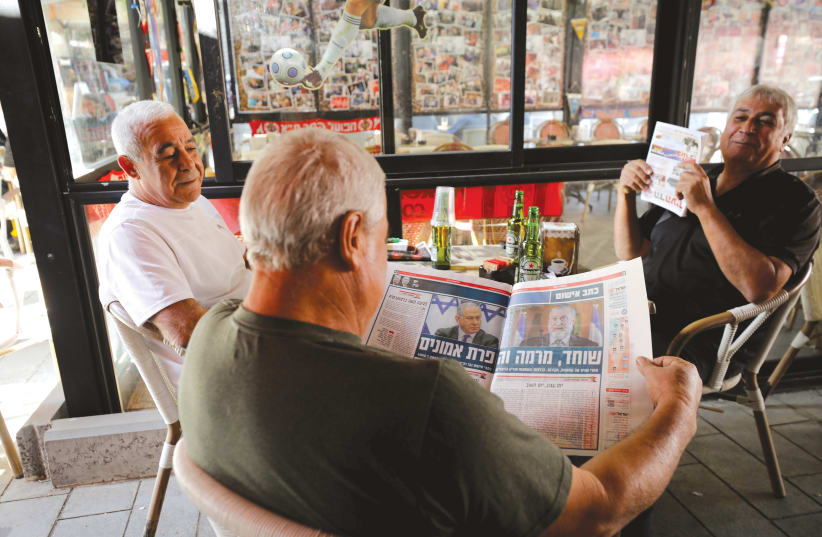 A man in a coffee shop in Ashkelon reads newspaper coverage of the prime minister's indictment last week.  (photo credit: AMIR COHEN/REUTERS)